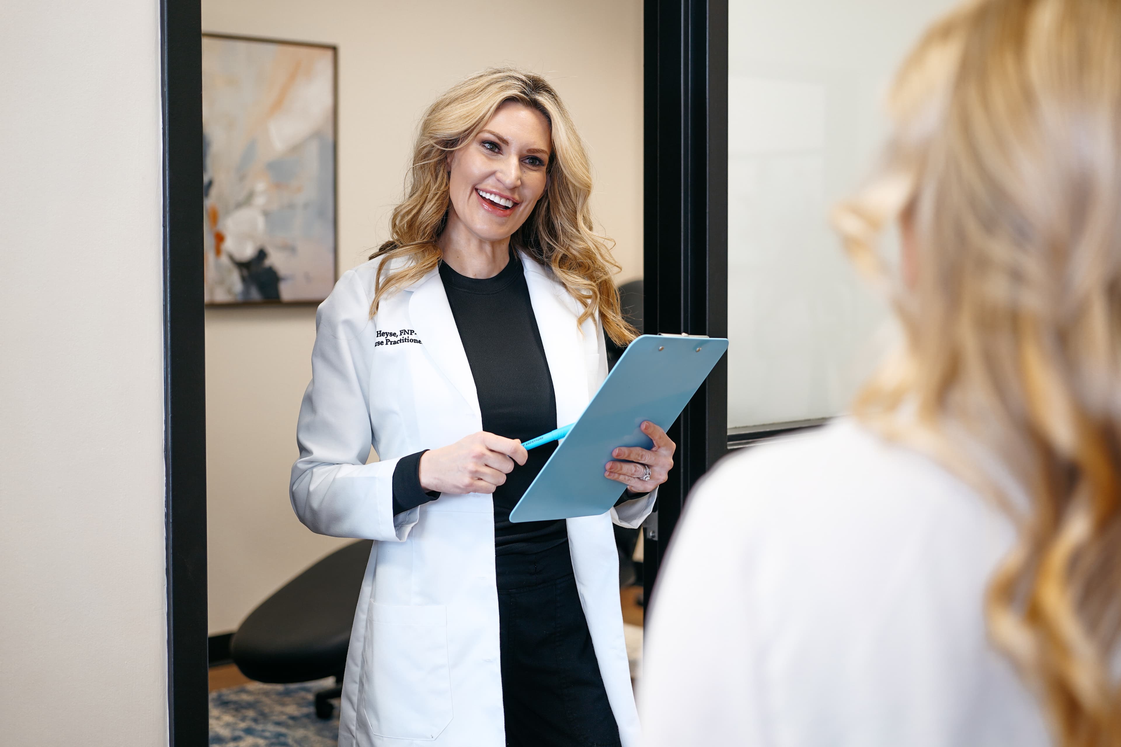 Nurse practitioner with a clipboard welcoming a guest into a treatment room